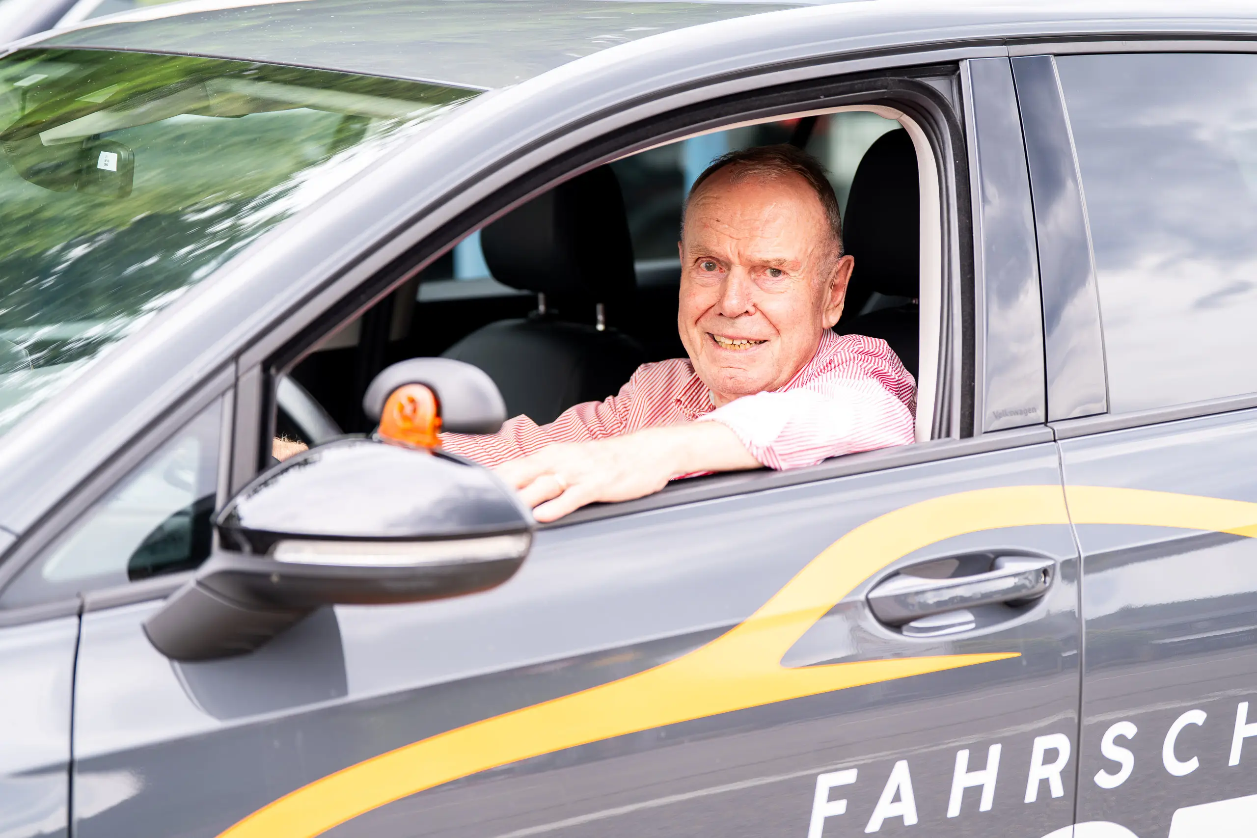 Älterer Herr in Fahrschulauto lächelt in Kamera